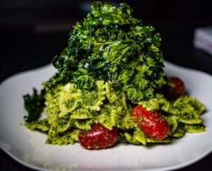 Bow tie pasta and cherry tomatoes with kale pesto topped with kale chips on a white plate