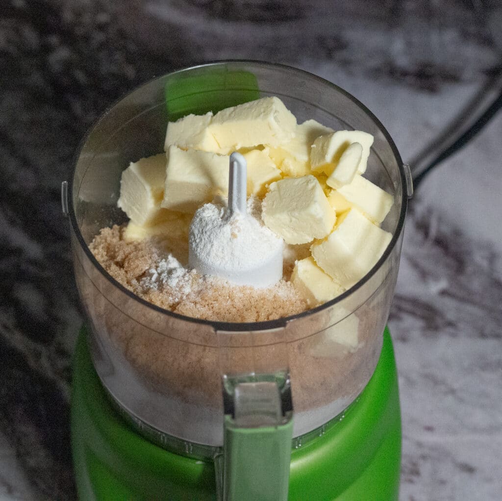 Chunks of butter, flour and brown sugar in a green mini food processor.